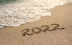 2022 written in the sand with a wave coming in