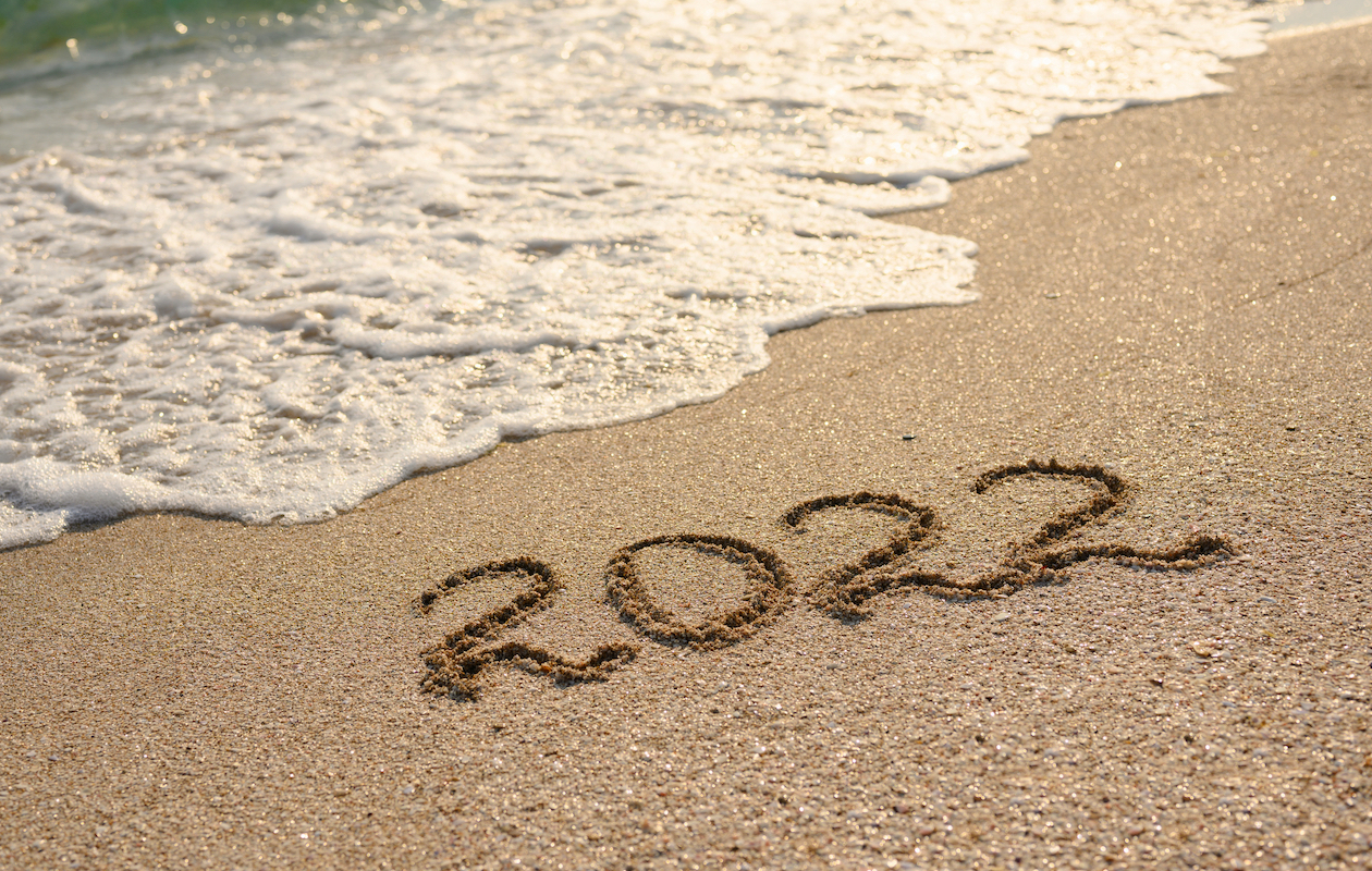 2022 written in the sand with a wave coming in