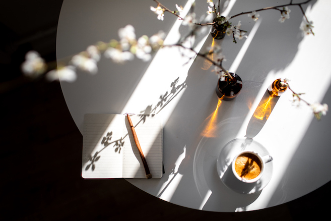 Small empty planner with coffee espresso and flowering cherry branches on white table in sunlight spring morning. How to start and planning perfect day.